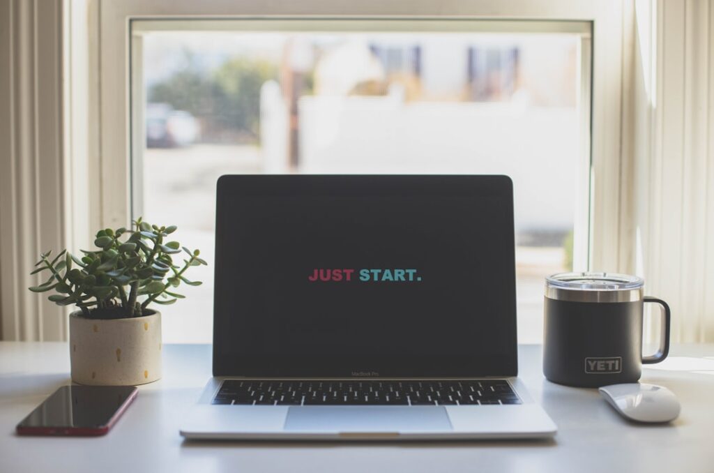 Clean workspace with laptop displaying 'JUST START' message, representing taking action and beginning new business initiatives
