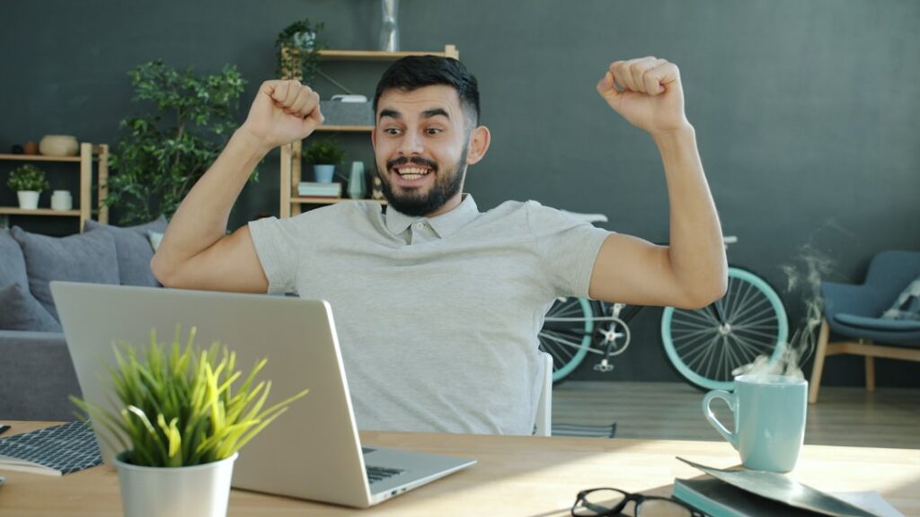 Excited business owner celebrating success with laptop representing the achievement of replacing expensive content agencies with AI tools