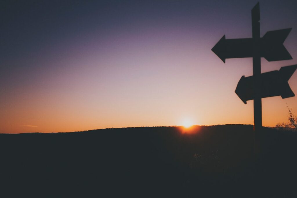 Directional signpost silhouetted against a sunset sky representing decision making and choosing the right path