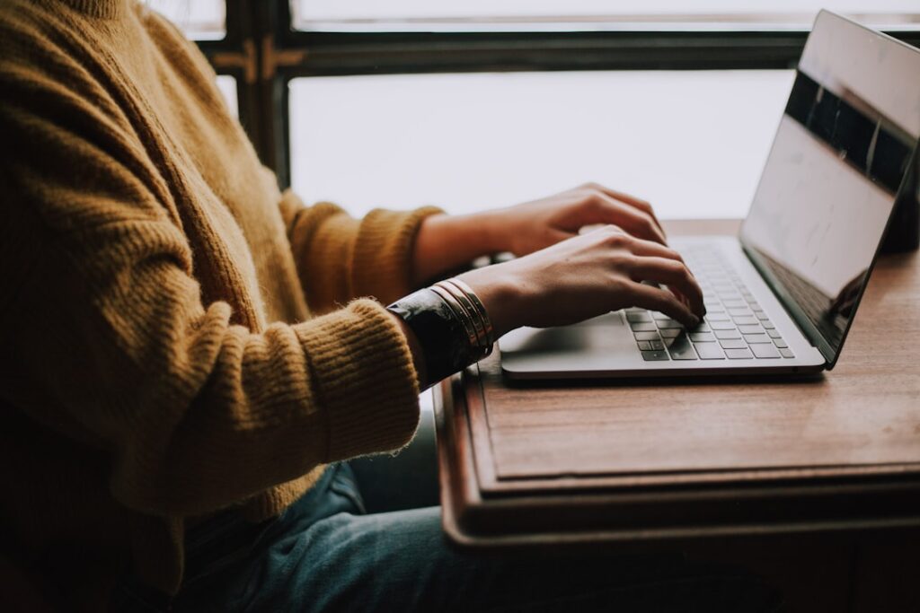 Person in a warm sweater typing and editing content on a laptop, representing human editorial review of AI-generated writing