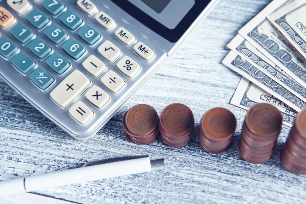 Calculator, stacked coins, and dollar bills on a desk representing SaaS pricing comparison and budget planning.