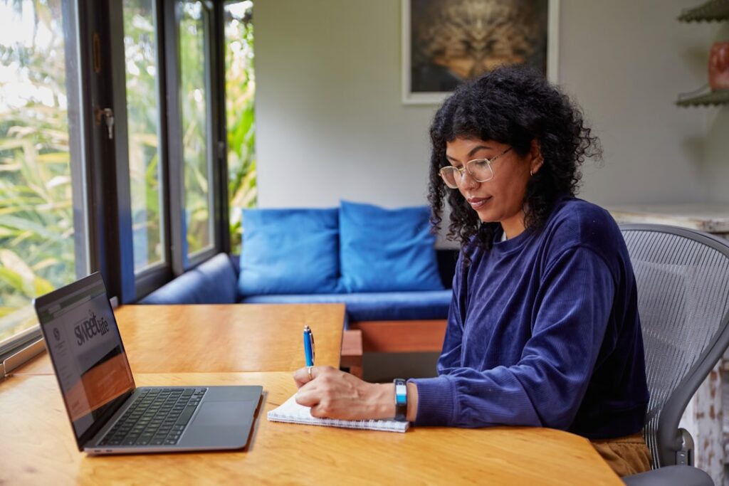 Solopreneur working at a laptop and taking notes, deciding when to use AI writing tools versus hiring a human writer.