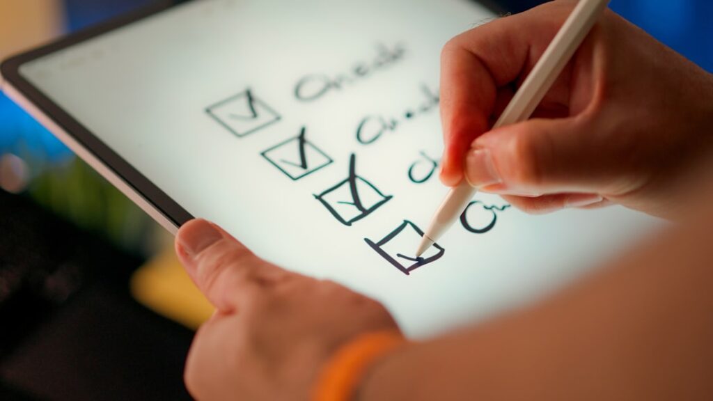 Person using stylus to check off items on digital tablet checklist, representing actionable steps for implementing AI blog writing tools