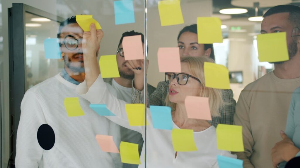 Small marketing team brainstorming with sticky notes on a glass wall, illustrating collaborative AI-assisted content workflows.