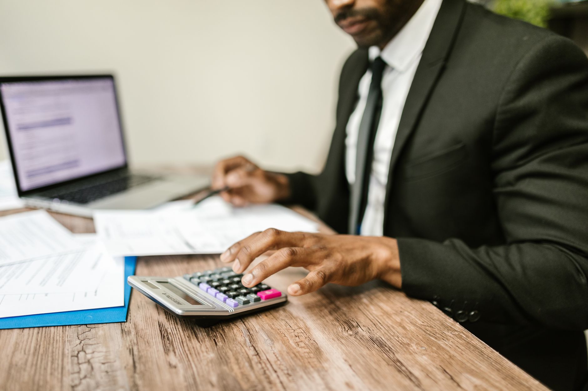 Accountant in a suit using a calculator with financial documents and laptop on desk