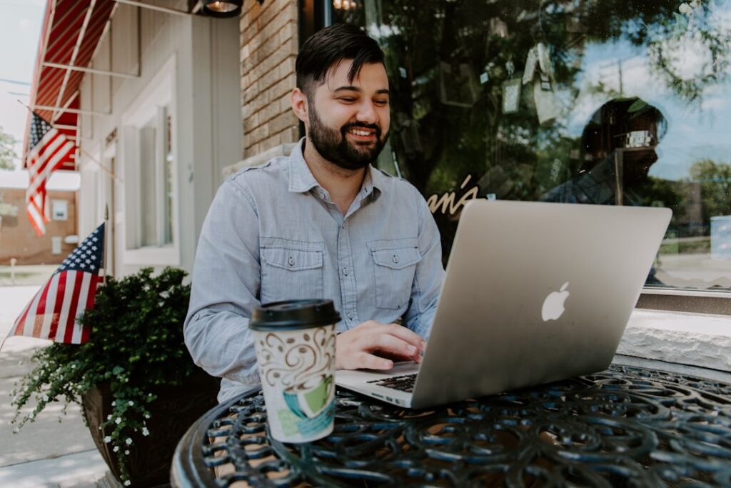 Freelance writer smiling while working on a MacBook at an outdoor cafe table