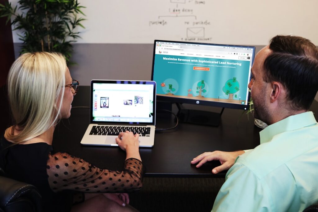 Two people reviewing and comparing AI writing tools on laptop and monitor screens side by side