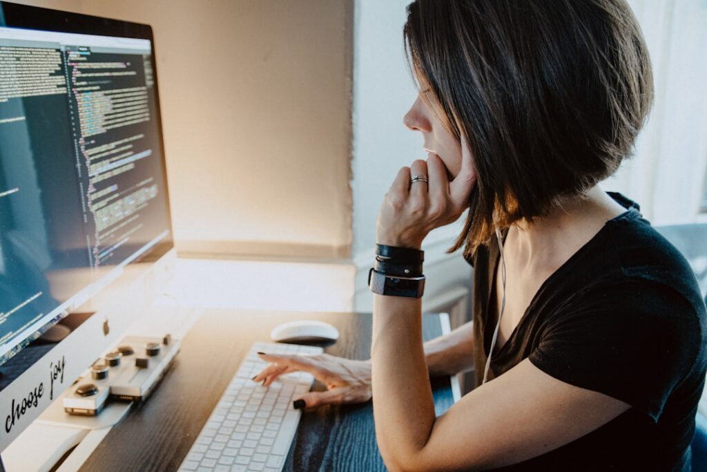 Woman sitting at a desk thinking carefully while looking at code on a computer screen