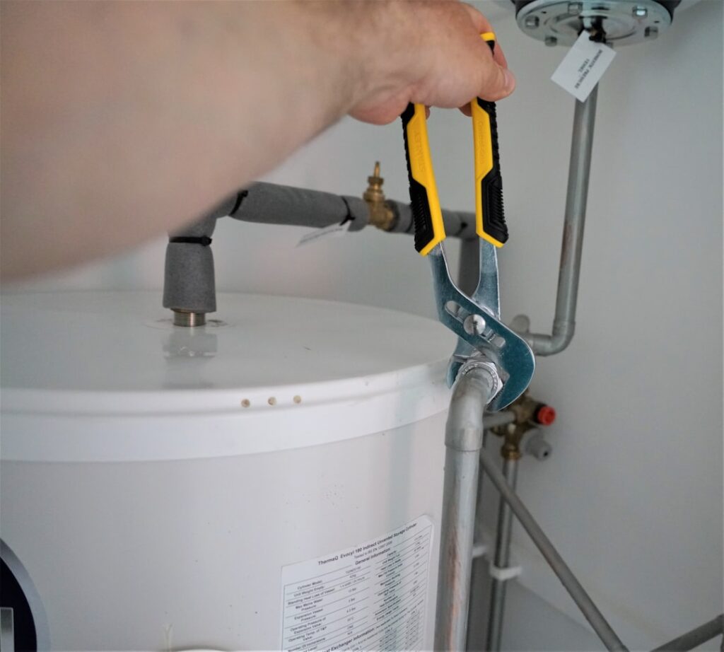 Plumber using a wrench on water heater pipe fittings during a service call
