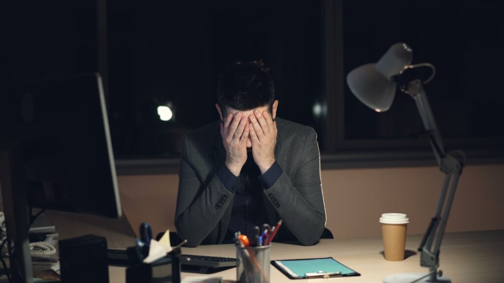 Stressed man with head in hands at his desk late at night, representing the pain of inconsistent content publishing and broken workflows