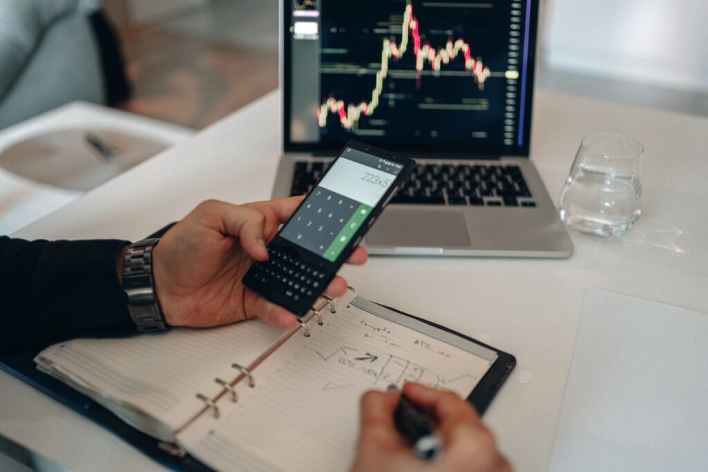 Person using a calculator and reviewing financial charts on a laptop, representing per-article cost calculation for AI writing tools