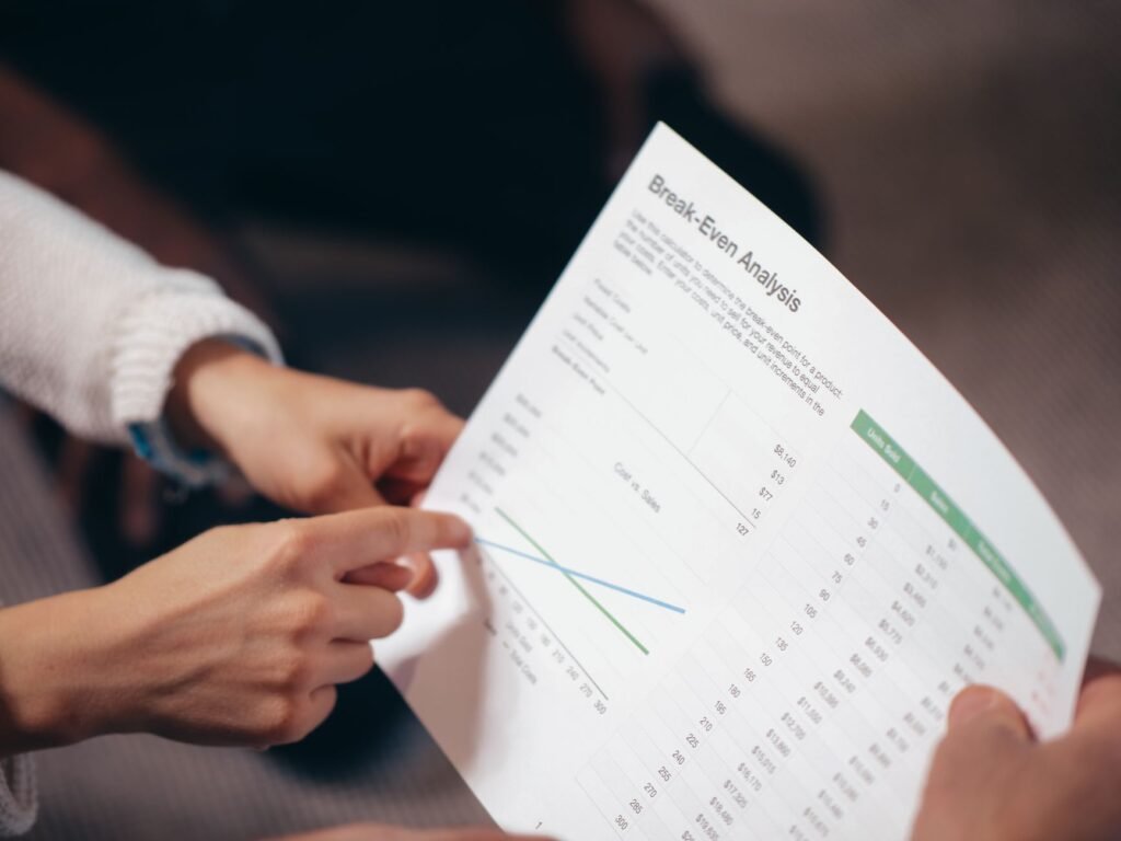 Hands reviewing a break-even analysis document with a cost-versus-sales chart, representing Frase pricing break-even by articles per month