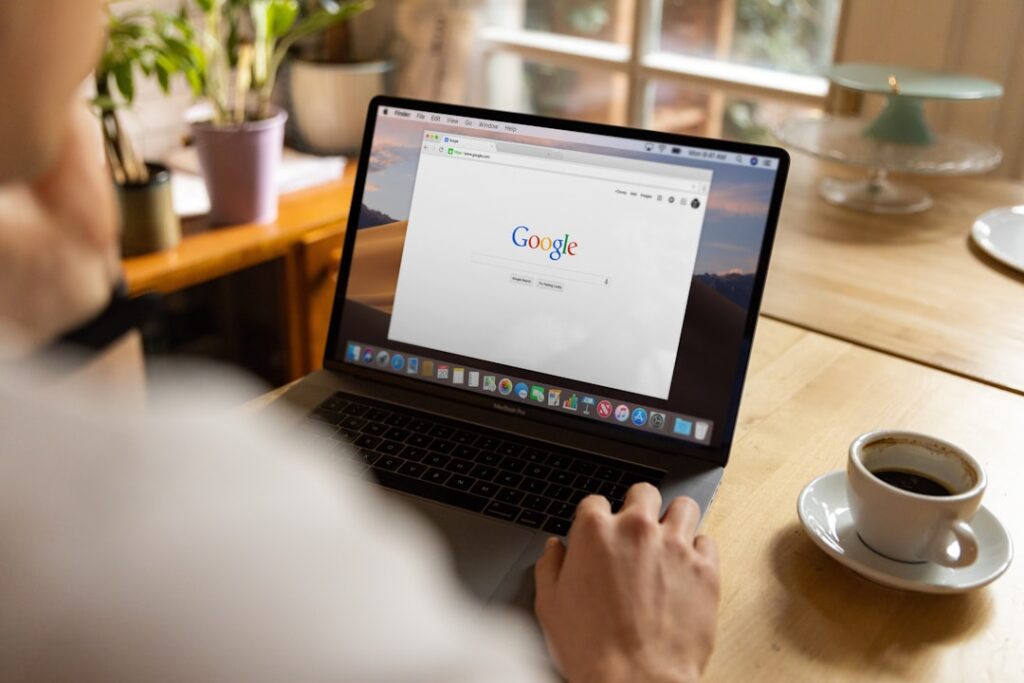 A person actively searching Google on a MacBook over a cup of coffee, representing the human-driven work of building brand, earning links, and developing genuine expertise that no plugin can automate