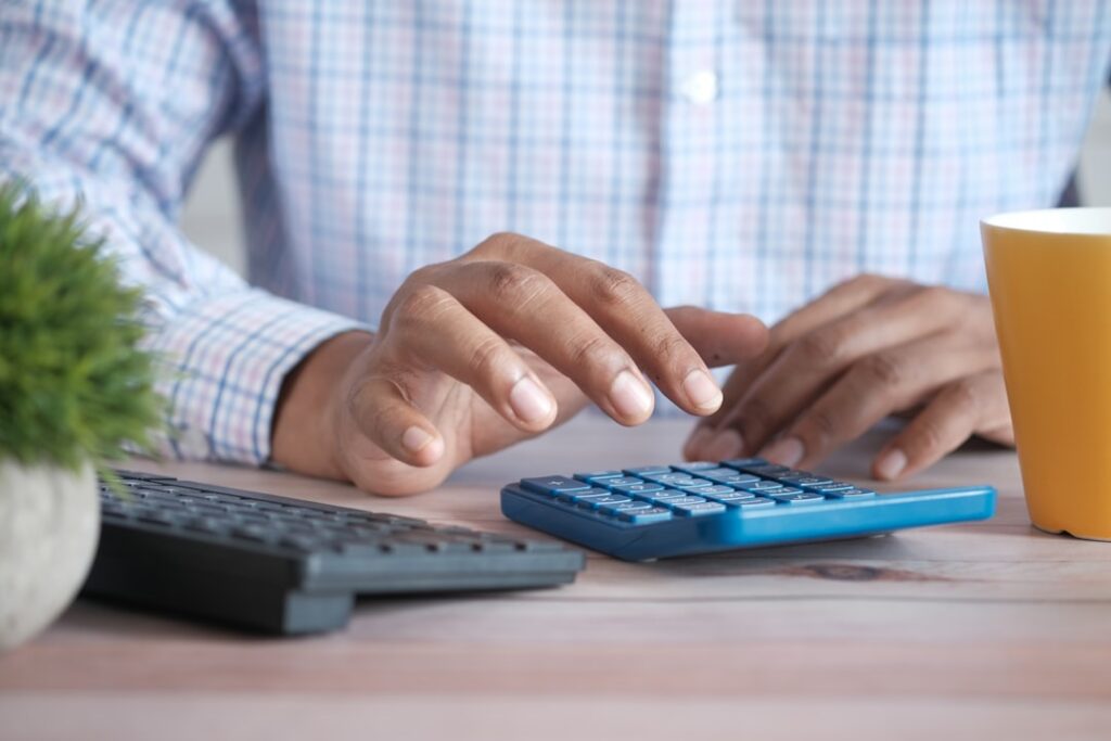 Person using a calculator at a desk to work out cost per article, representing ContentBot pricing math.
