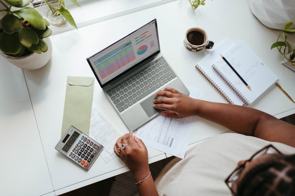 Business owner reviewing marketing budget and financial charts on a laptop with a calculator, illustrating the cost comparison between content agencies and auto blogging plugins.