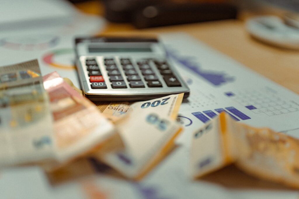 Calculator sitting on top of banknotes and budget reports, representing the real cost-per-article calculation including both tool cost and labor cost for AI content publishing.