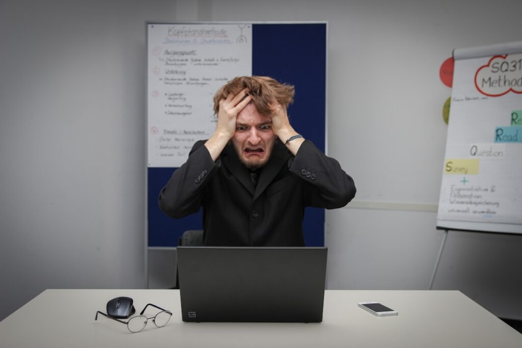 Frustrated business owner with head in hands in front of laptop — overwhelmed by high marketing agency costs