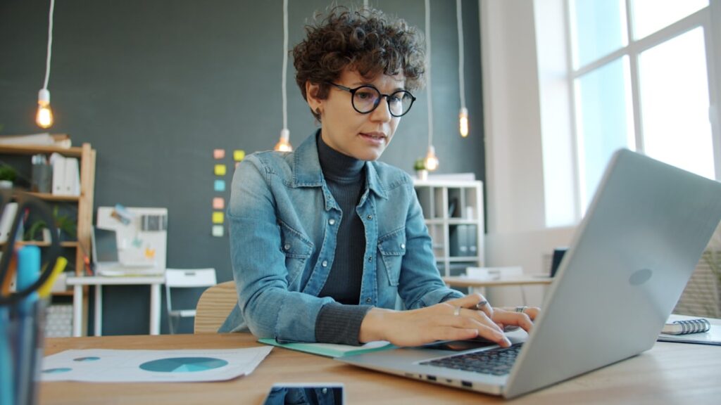 Focused woman wearing glasses working on a laptop in a modern office, representing editorial review of AI-assisted content