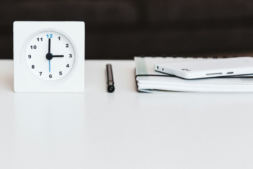 White desk clock next to a notepad and pen representing time tracking for content workflows