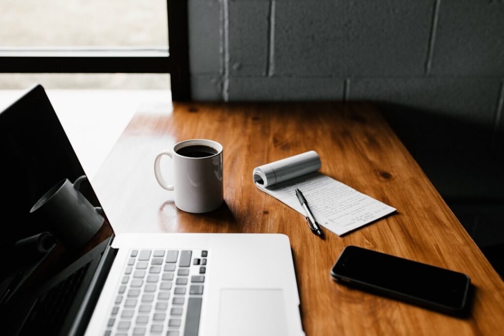 Laptop, coffee mug, notepad, and phone on a wooden desk representing blog content strategy and writing workflow