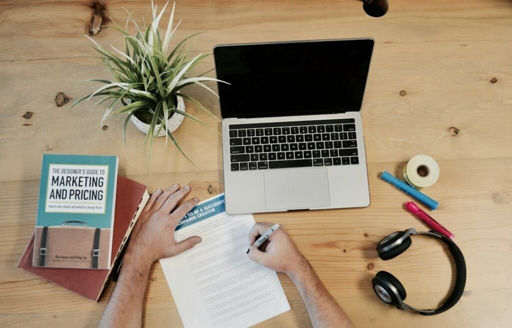 Marketing flatlay with laptop, marketing and pricing book, and notepad representing content marketing workflow options