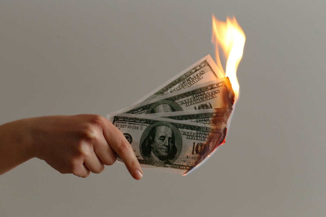 Hand holding burning $100 dollar bills representing wasted Google Ads budget for small businesses. Photo by Jp Valery on Unsplash.