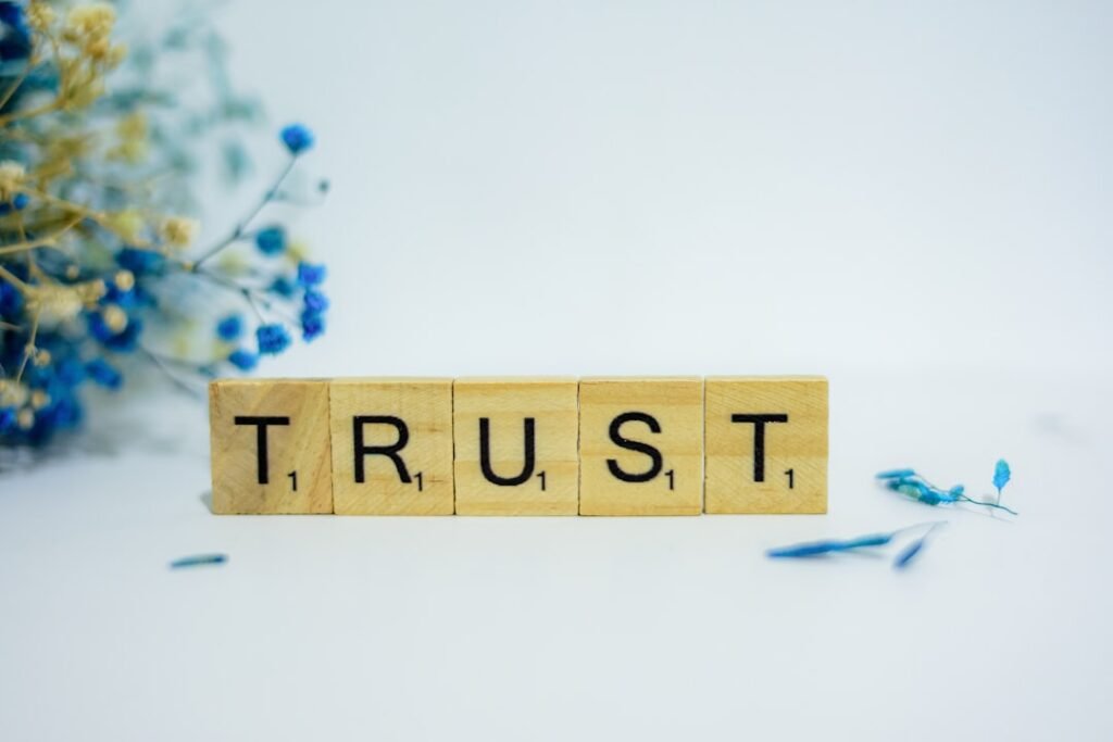 Wooden scrabble tiles spelling the word TRUST surrounded by blue flowers, representing reader trust and publisher credibility