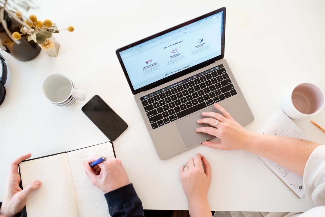 Two people collaborating on content strategy with a laptop and notebook on a white desk