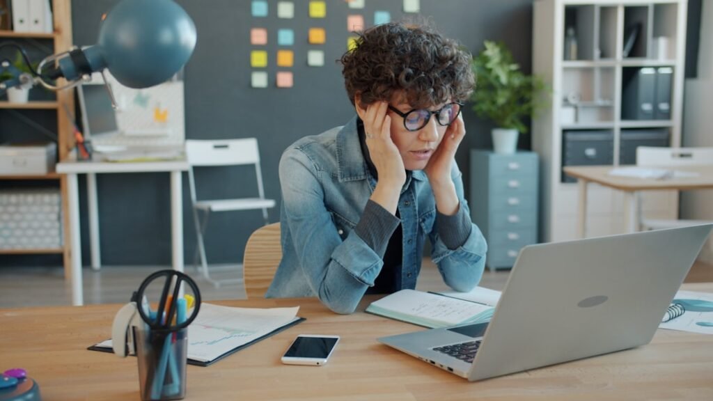 Frustrated marketer with head in hands at laptop, overpaying for software tools they barely use