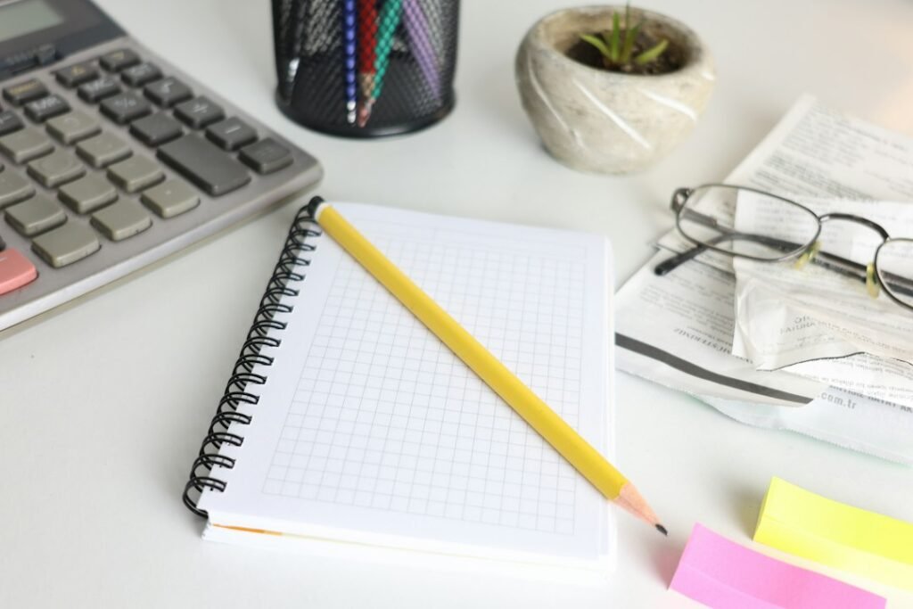 Calculator, graph-paper notebook, and glasses on a desk, representing per-output cost analysis for AI marketing tools