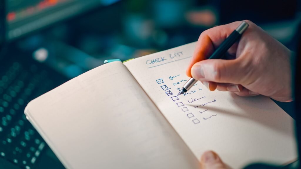 Hand writing a step-by-step checklist in a notebook next to a computer, representing a content refresh workflow with a human approval gate
