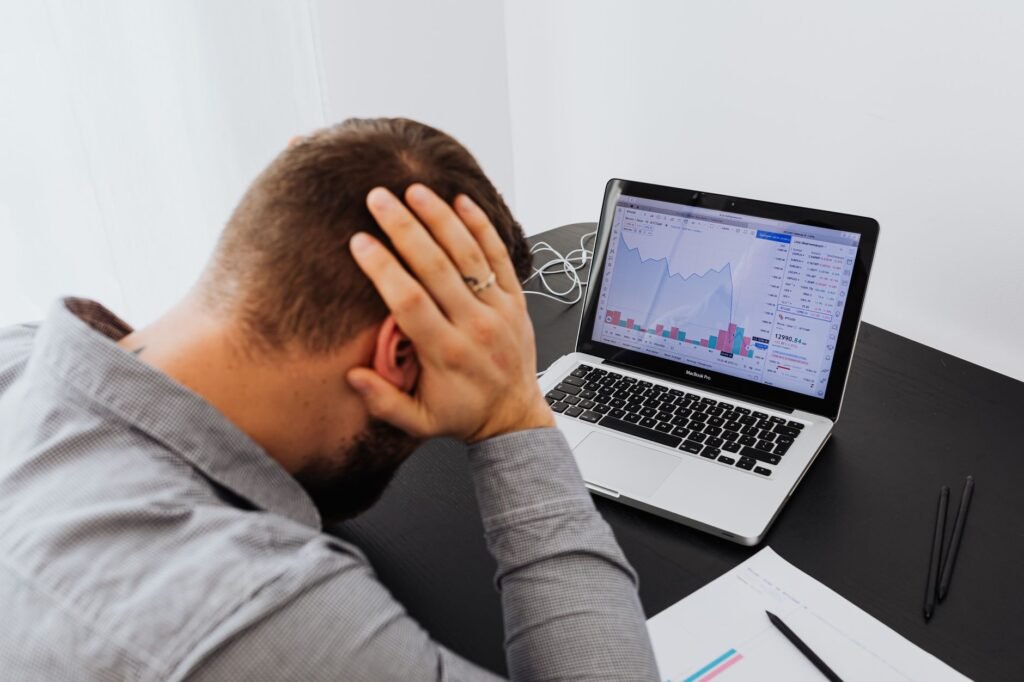 Stressed person at desk with head in hands looking at a laptop showing declining data charts, representing the impact of keyword research mistakes on traffic and budget.