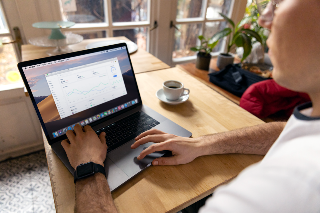 Person reviewing blog analytics and traffic trend charts on a laptop at a cafe table with coffee