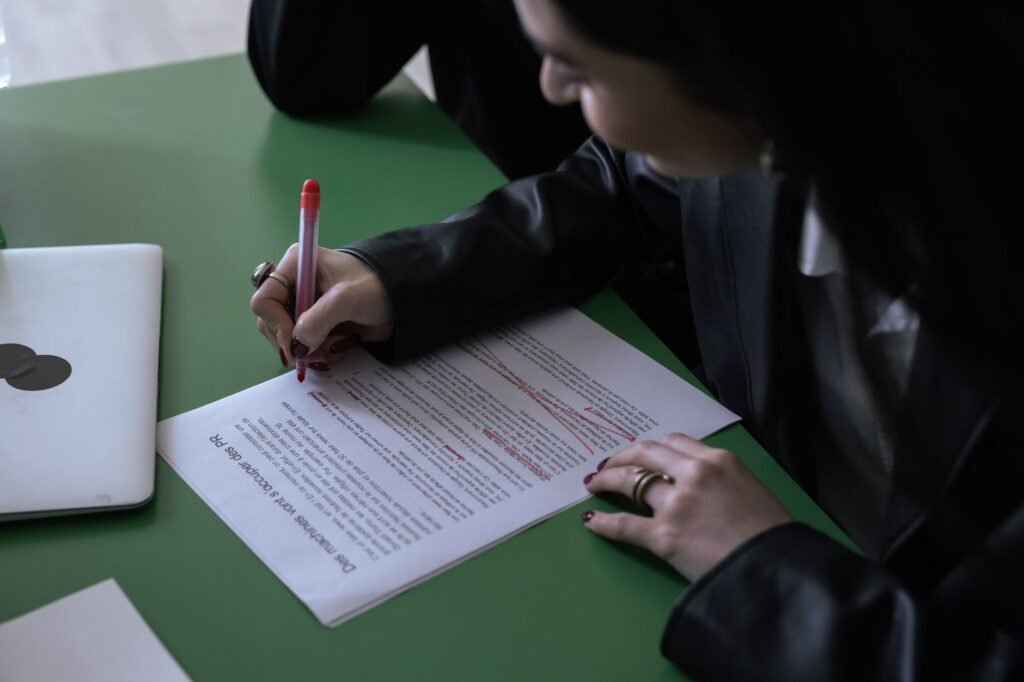 Person editing a printed document with a red pen, marking up text for revision and restructuring