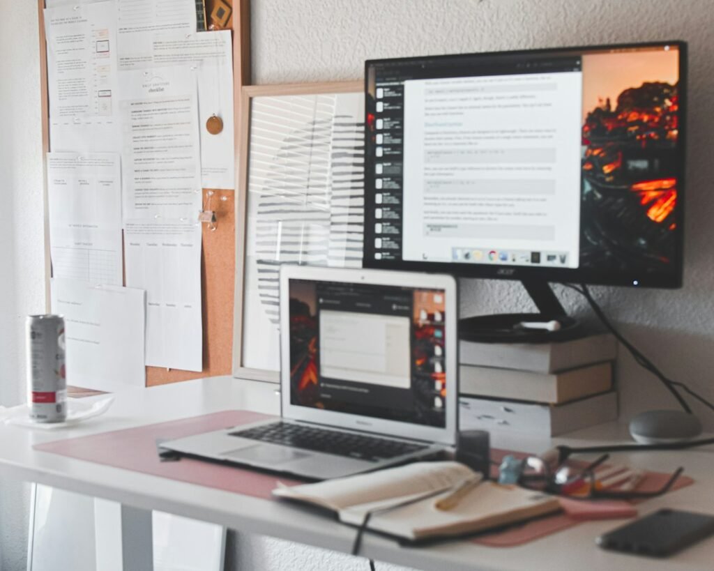 Writer's desk with dual monitors showing text documents and a pinboard of printed notes in the background