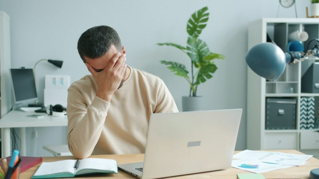 Frustrated small business owner sitting at laptop with head in hands, overwhelmed by poor SEO rankings despite following best practices