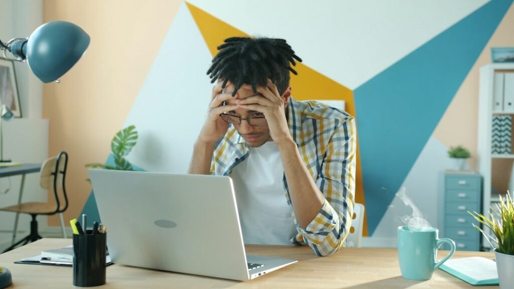 Stressed small business owner with head in hands looking at an overwhelming analytics dashboard on a laptop screen