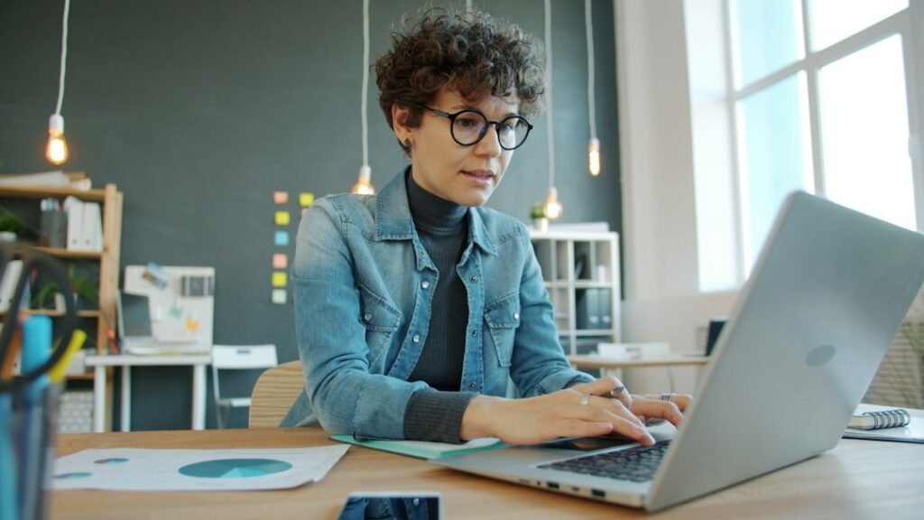 A content marketer reviews and edits AI-generated drafts at her laptop before approving them for publication, illustrating the human approval gate principle.